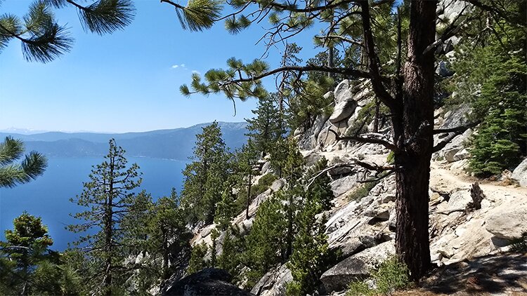 Photo from the trail overlooking Lake Tahoe far below with Sierra Nevada mountains in the background.